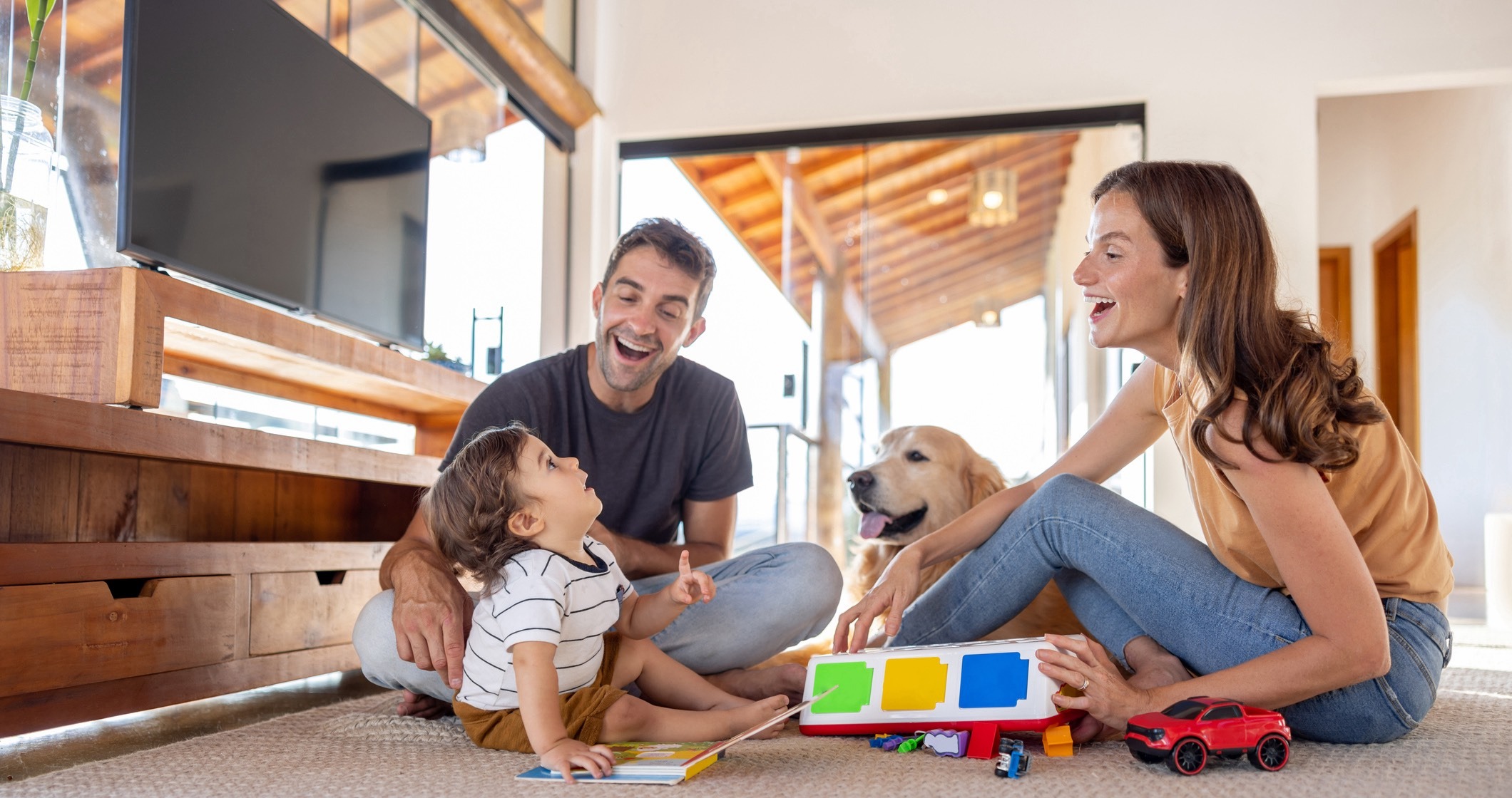 A happy family with a young child and a golden retriever dog playing with toys on the living room floor, smiling and enjoying time together.