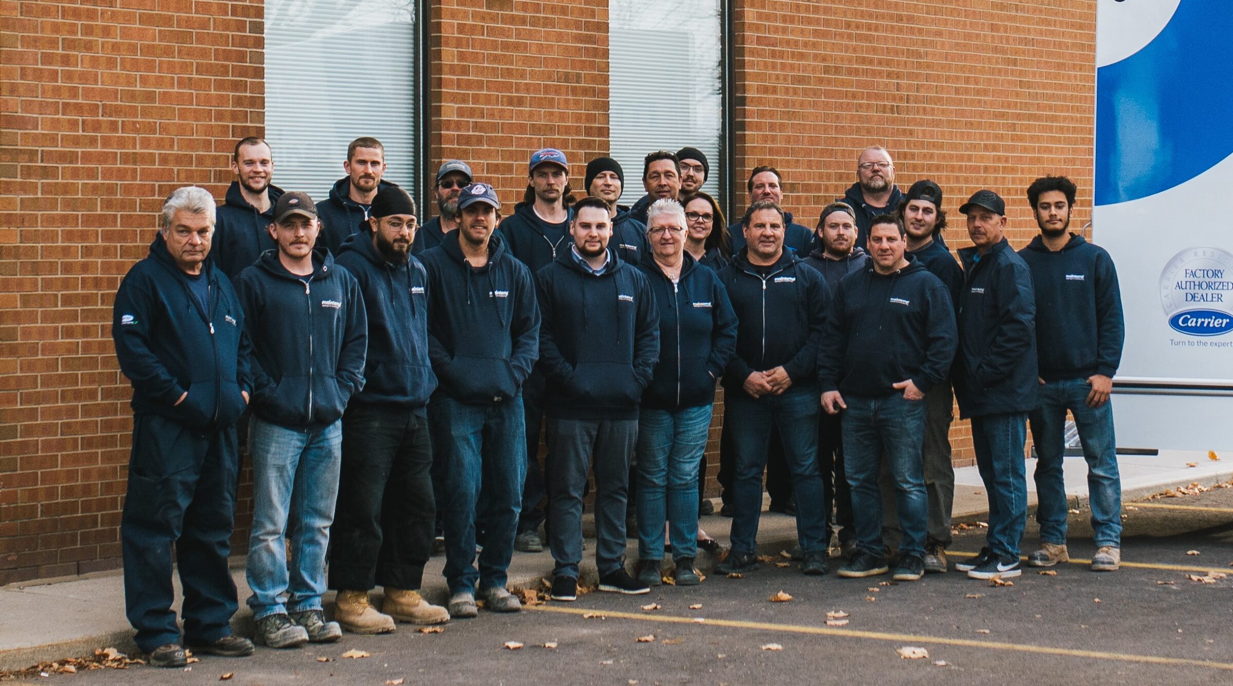 A group of people in matching blue work uniforms pose for a photo outdoors by a brick building, likely a team of service professionals.