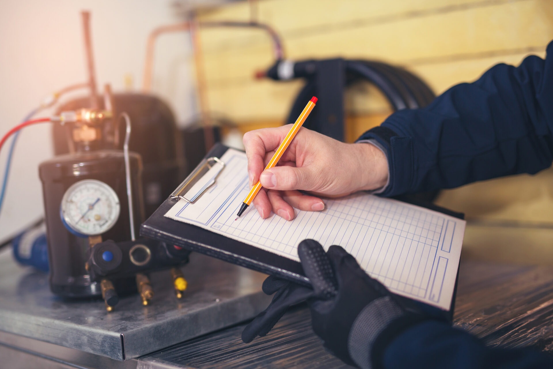 A person is writing on a clipboard with a pencil near HVAC equipment, possibly performing maintenance or checking system operations with focus on precision.