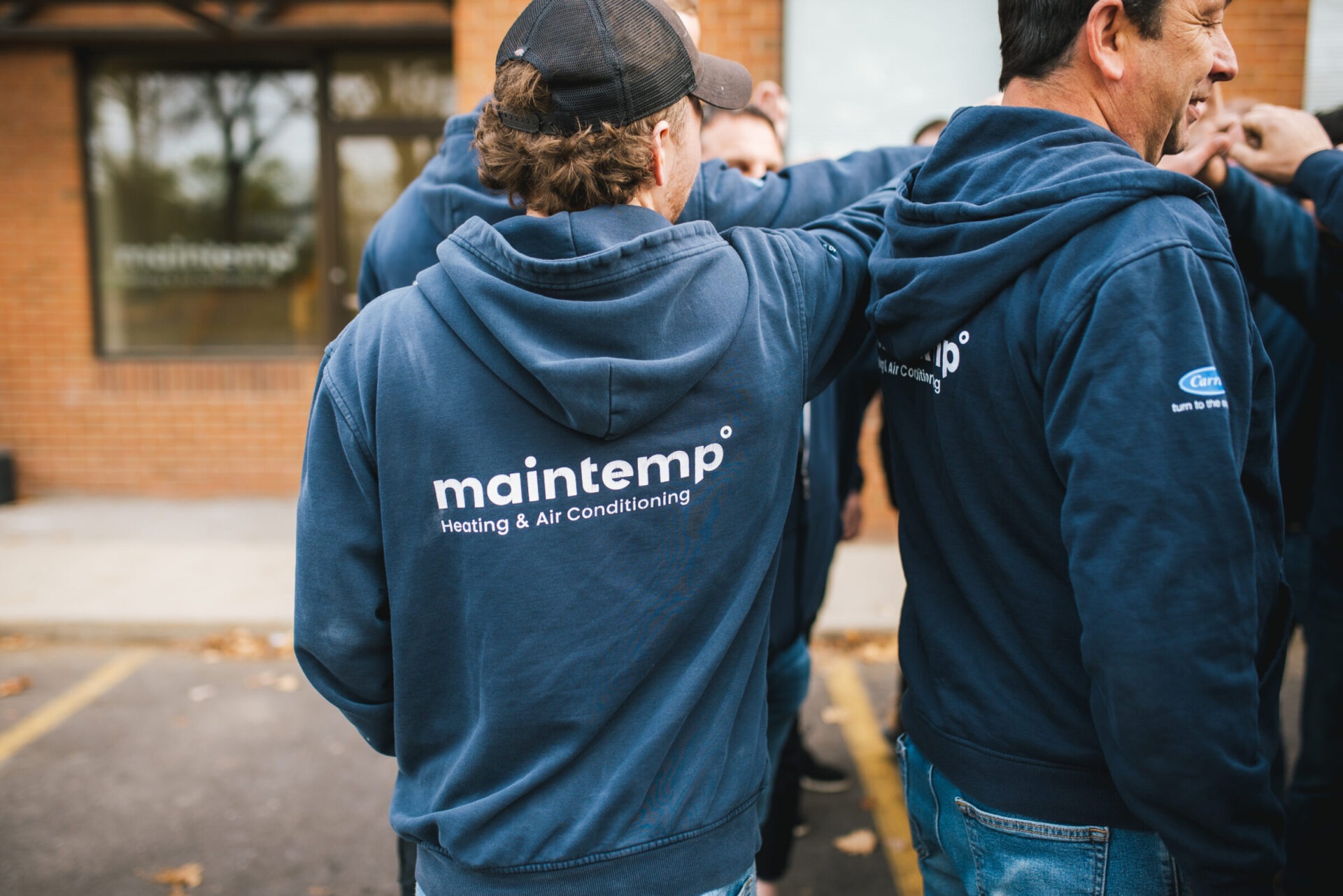 Several people in blue hoodies with "maintemp Heating & Air Conditioning" logos on them are standing together, fostering a sense of teamwork.