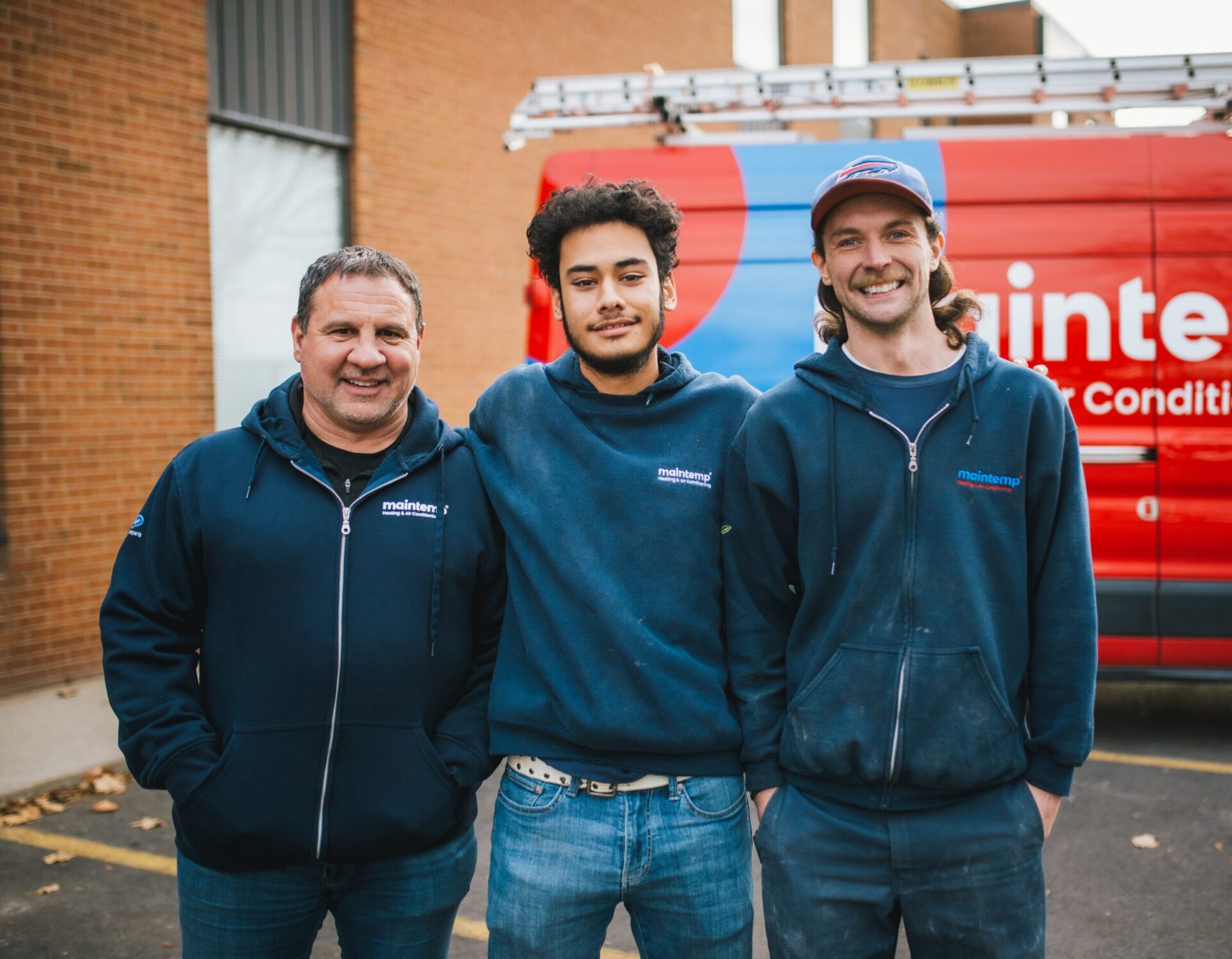 Three people in work uniforms stand smiling in front of a red van with "Maintenance & Conditioning" text. They look content and professional.