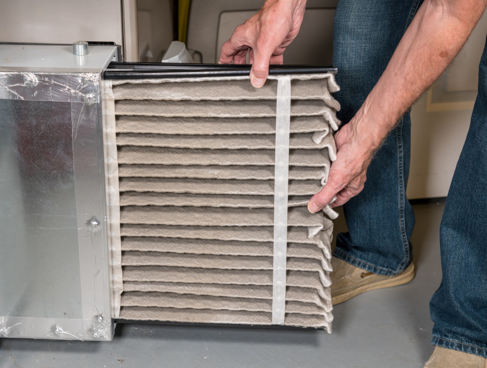 A person is installing a dirty furnace filter into an HVAC unit, demonstrating maintenance work, likely in a home or industrial setting.
