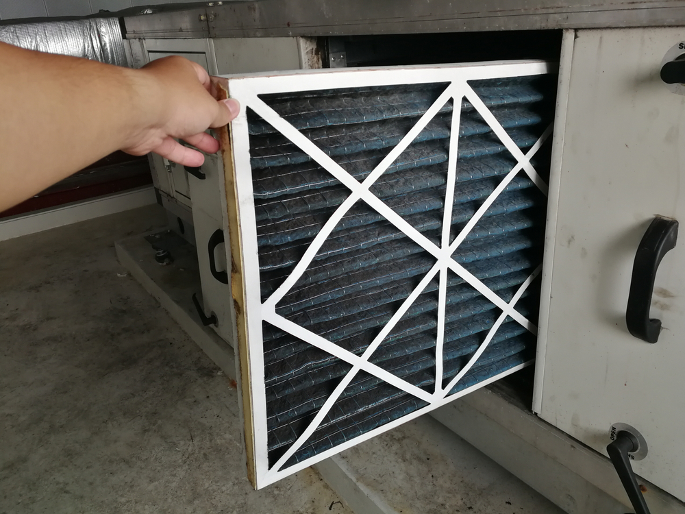 A person's hand is removing a dirty air filter from an HVAC unit, indicating maintenance or replacement of the filter for cleaner air circulation.